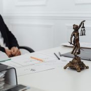 Mesa de trabalho com documentos jurídicos, laptop e uma estátua da Justiça
