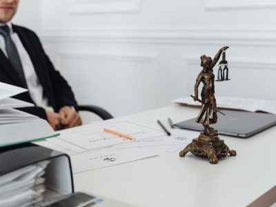 Mesa de trabalho com documentos jurídicos, laptop e uma estátua da Justiça