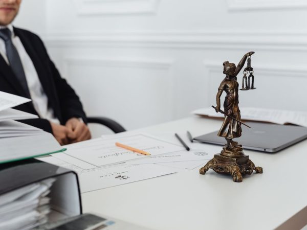 Mesa de trabalho com documentos jurídicos, laptop e uma estátua da Justiça