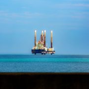 Plataforma de petróleo offshore vista à distância em meio ao oceano azul, sob céu claro.