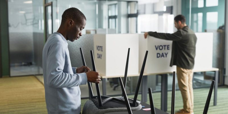 Homens organizam cabines de votação em uma seção eleitoral interna.