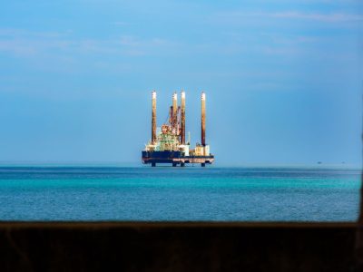 Plataforma de petróleo offshore vista à distância em meio ao oceano azul, sob céu claro.