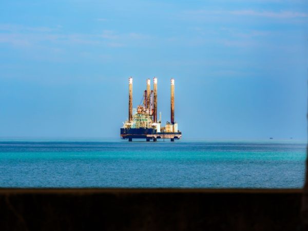 Plataforma de petróleo offshore vista à distância em meio ao oceano azul, sob céu claro.