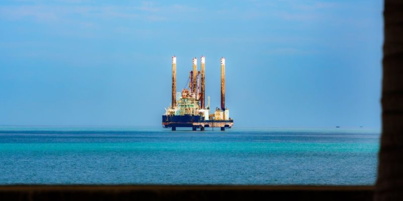 Plataforma de petróleo offshore vista à distância em meio ao oceano azul, sob céu claro.